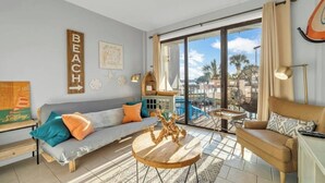 Ein geräumiges Wohnzimmer mit großem Fenster, einer Couch, einem Couchtisch und einem Balkon mit Blick auf Palmen.