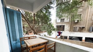 Ein Balkon mit Holztisch und Stühlen, eine blaue Tür und Blick auf ein Gebäude, an dem Wäsche aufgehängt ist.