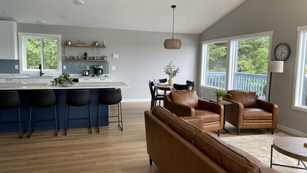 A modern kitchen with a bar area, a dining set, and a leather sofa in a bright living room with large windows. - Nordic House (Petersburg)