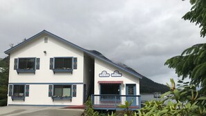 A two-story building with a white facade and blue trim, featuring a porch with a bench and a small garden area. - Nordic House (Petersburg)