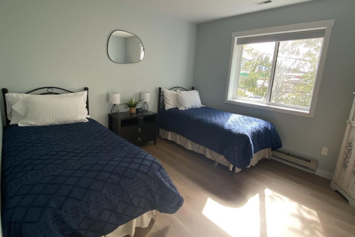 A bedroom with two beds, a bedside table, a mirror, and a window.