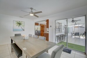 Ein Essbereich mit Holztisch, Stühlen und Deckenventilator. Es gibt eine Küchenzeile mit Holzausbau und einem Kühlschrank.