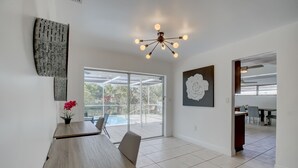 Una habitación amplia con una mesa de comedor de madera, una lámpara moderna y un gran ventanal con vistas a una piscina.