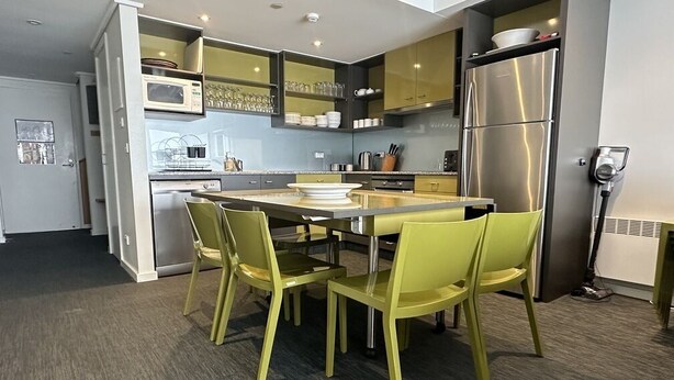Een moderne keuken met een eethoek, met een koelkast van roestvrij staal, een magnetron en een eettafel met gele stoelen.