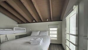 Een slaapkamer met een groot bed, een raam met jaloezieën, een nachtkastje en een houten plafond.