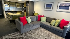 Een moderne woonkamer met een grijze modulaire bank, een eettafel met stoelen, een keukenhoek en twee ingelijste foto’s aan de muur.