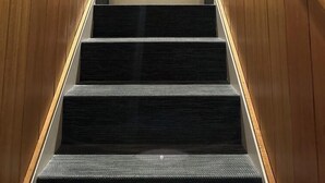 Een houten trap met een leuning, beklede treden en een ingelijst beeld boven de bovenste trede.