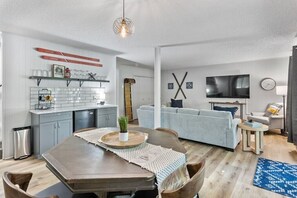 Una sala de estar moderna con un sofá gris, un televisor y un comedor con una mesa de madera y sillas.