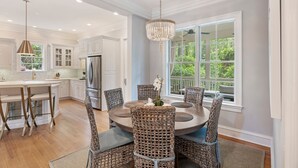 A spacious kitchen with white cabinetry, a large island, and a dining area with wicker chairs.