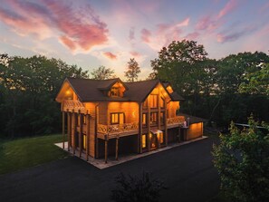 A two-story log cabin with a balcony and a porch, surrounded by trees. - Log House Vacation Rental with Pool and Sauna (Pocono Township)