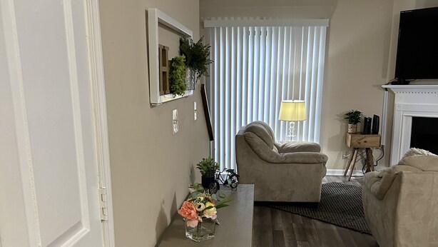 Sala de estar com piso de madeira, um sofá bege, uma mesinha com um vaso de flores e uma lareira.