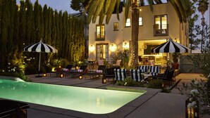 Un espace aménagé au bord de la piscine, avec des chaises longues et des parasols, une piscine, et un bâtiment doté de nombreuses fenêtres et de balcons.