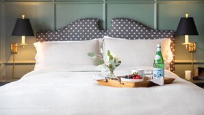 Un lit bien fait, avec du linge de lit blanc, un plateau avec une bouteille d’eau et un bol de fruits.