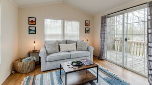 A living room with a grey sofa, a coffee table, and a large window with blinds. - Story-time Stay at Our Rupert Cottage! (Monteagle)