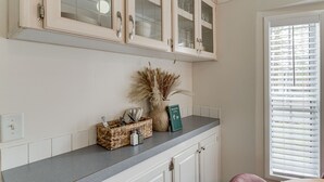 Uma cozinha com armários brancos, bancada de granito e janela com persianas.