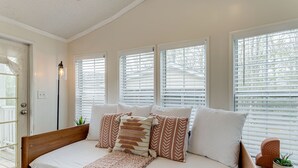 Quarto com cama de madeira, roupa de cama branca e várias janelas com persianas.