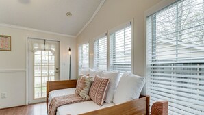Quarto com cama de madeira, roupa de cama branca e várias janelas com persianas.