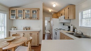Cozinha moderna com armários de madeira, bancada branca e área de refeições com mesa e cadeiras.