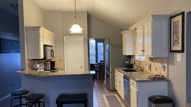 A modern kitchen with a central island, bar stools, a refrigerator, and a microwave. - Adorable Home Away From Home in the City by the Bay (Corpus Christi)
