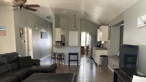 A living room with a sofa, a TV, and a ceiling fan. There is a kitchen area with cabinets and a microwave. - Adorable Home Away From Home in the City by the Bay (Corpus Christi)