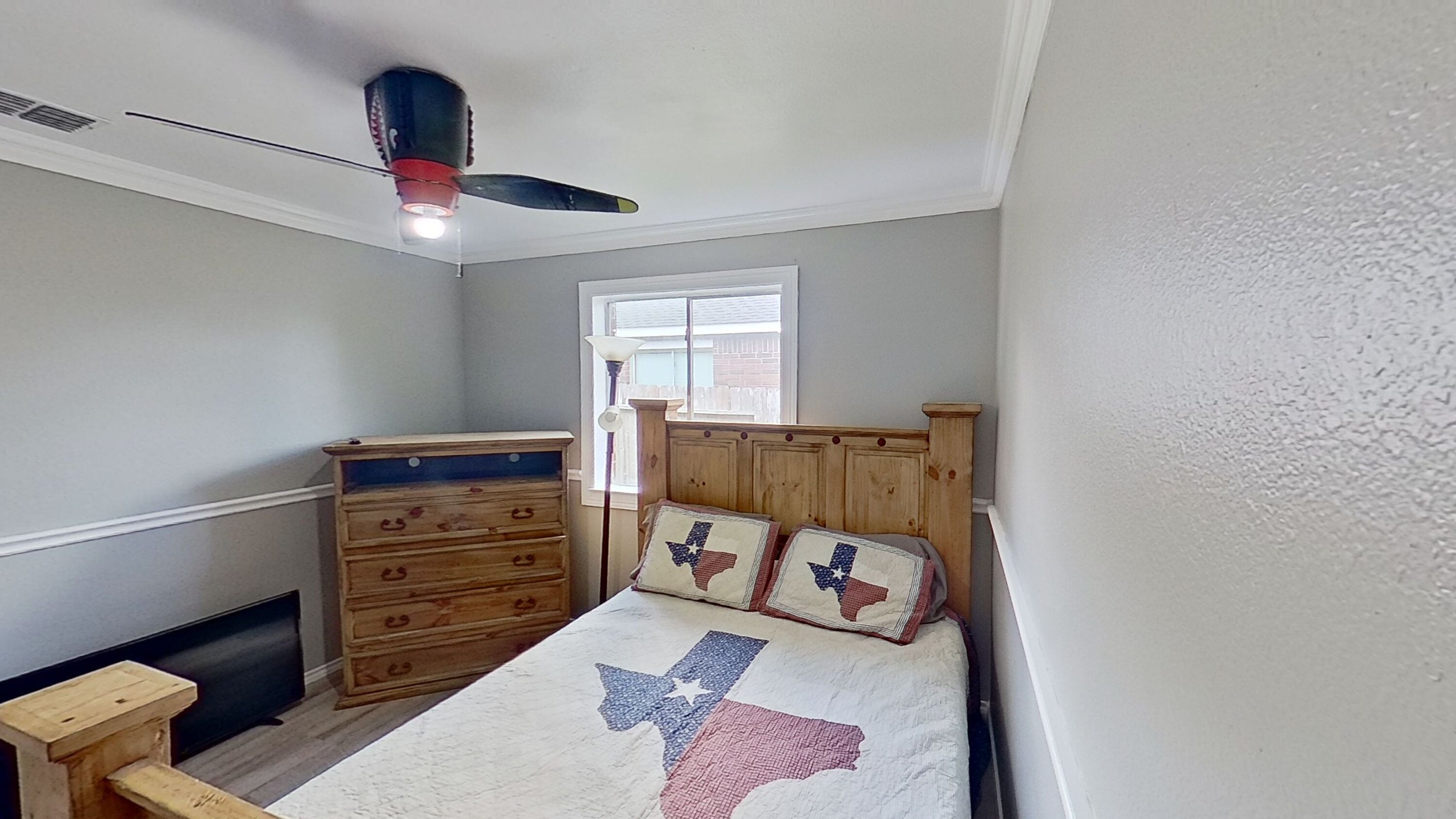 A bedroom with a bed featuring a Texas flag quilt, a wooden dresser, and a ceiling fan.