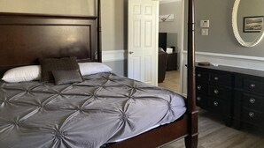 A four-poster bed with a tufted headboard, a dresser with multiple drawers, and a mirror on the wall. - Adorable Home Away From Home in the City by the Bay (Corpus Christi)