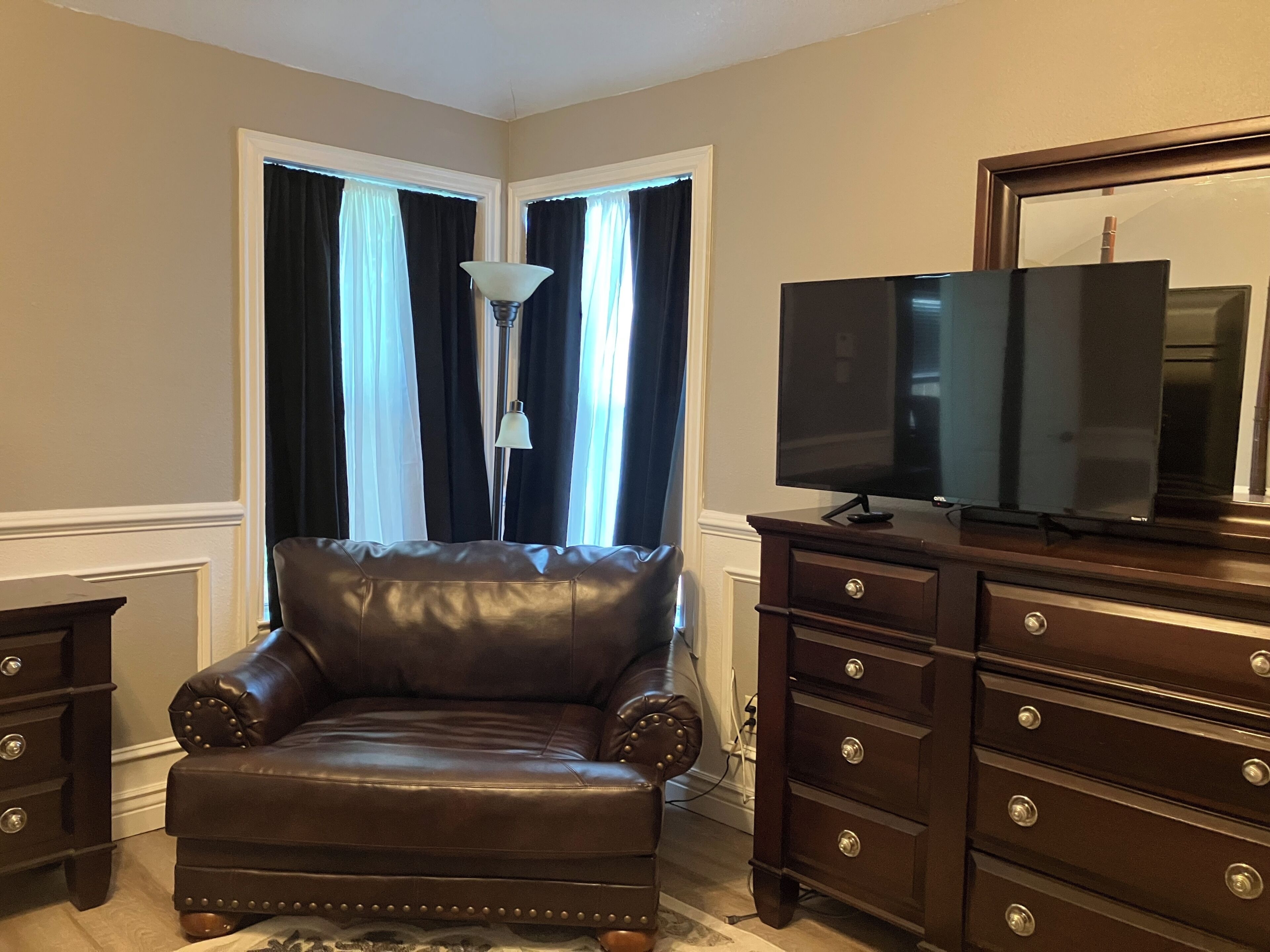 Una habitación con un sillón de cuero, un televisor sobre un mueble de madera y una lámpara.