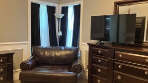 A room with a leather armchair, a TV on a wooden cabinet, and a lamp. - Adorable Home Away From Home in the City by the Bay (Corpus Christi)