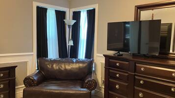Una habitación con un sillón de cuero, un televisor sobre un mueble de madera y una lámpara.