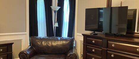 A room with a leather armchair, a TV on a wooden cabinet, and a lamp.