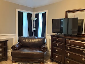 Una habitación con un sillón de cuero, un televisor sobre un mueble de madera y una lámpara.