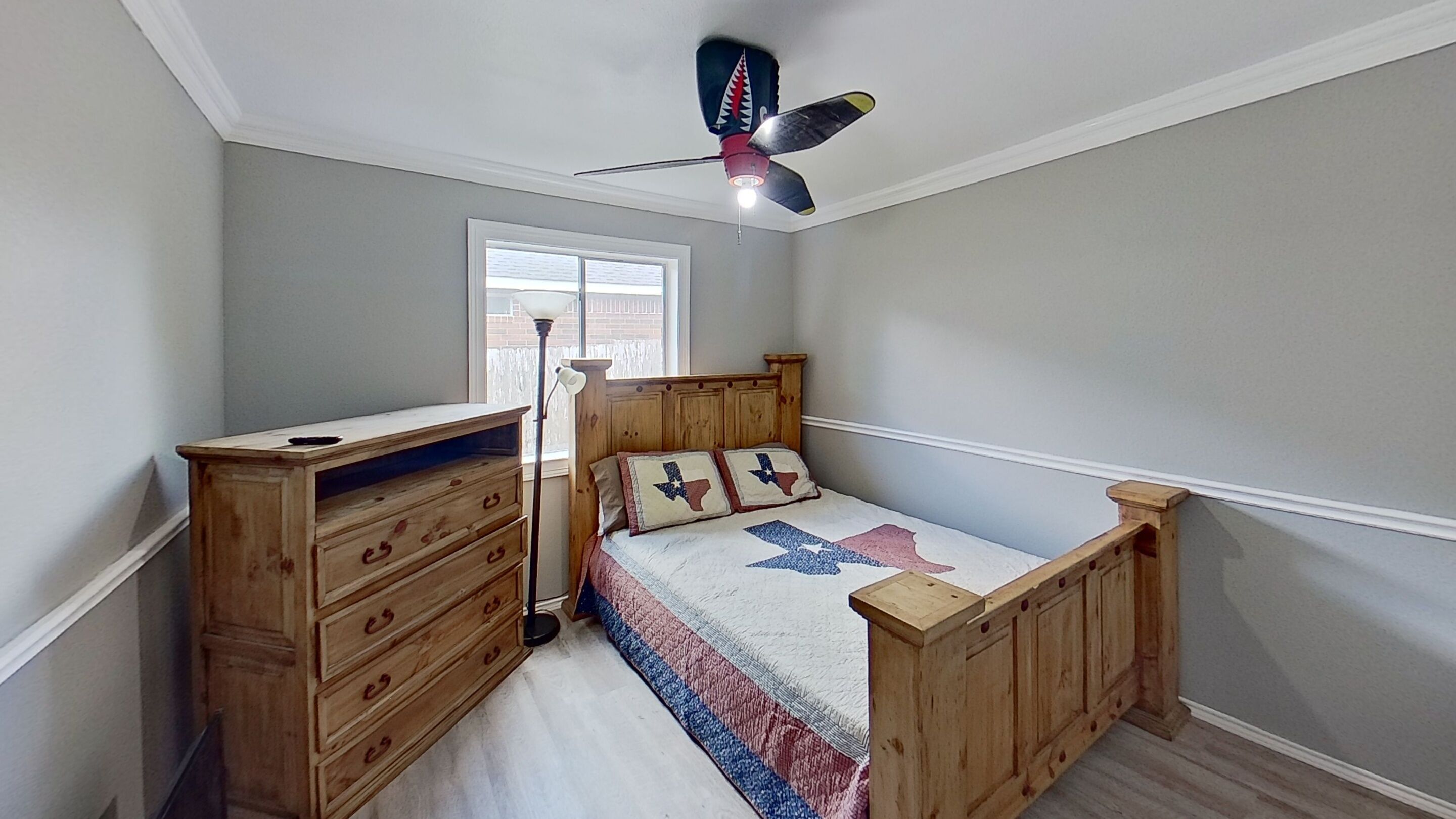 Een slaapkamer met een houten bed, nachtkastje, dressoir en plafondventilator.