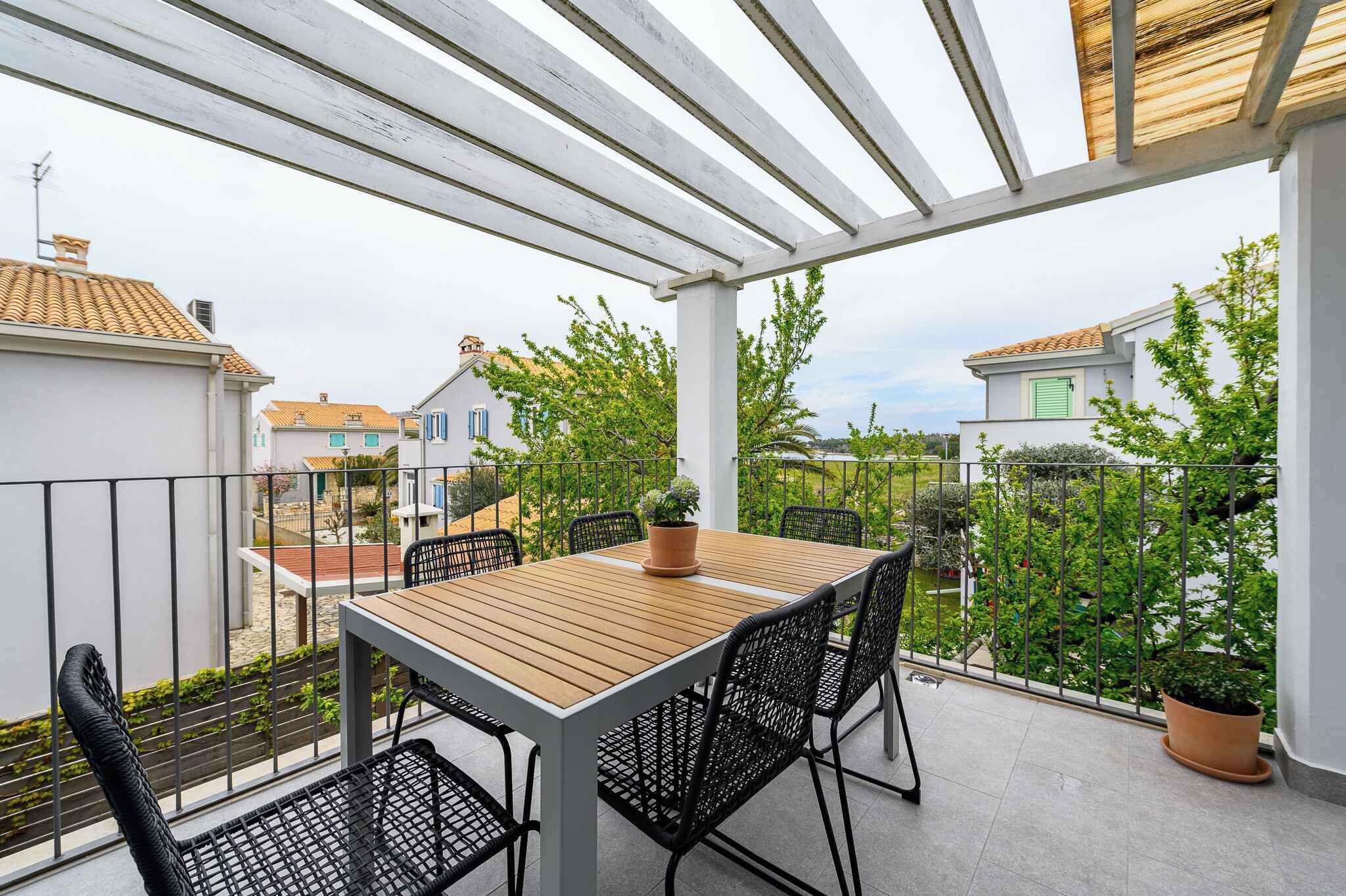 En overdækket balkon med et træbord og stole, plantekasser og udsigt til omkringliggende huse.