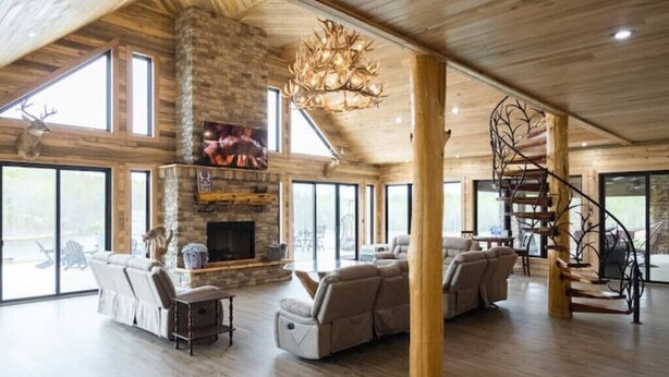 A spacious living room with a stone fireplace, large windows, and a wooden ceiling. - Possum Pocket Lodge
 (Nortonville)