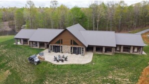 A large, modern building with a central wooden section and stone walls, surrounded by a well-maintained lawn and a body of water. - Possum Pocket Lodge
 (Nortonville)
