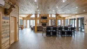 A spacious room with wooden floors and walls, a fireplace, a dining area with chairs, and large windows. - Possum Pocket Lodge
 (Nortonville)