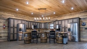 A rustic kitchen with wooden cabinets, stainless steel appliances, and a central island with bar stools. - Possum Pocket Lodge
 (Nortonville)