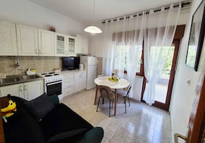 A compact kitchen with a dining area, a sofa, and a window with curtains.