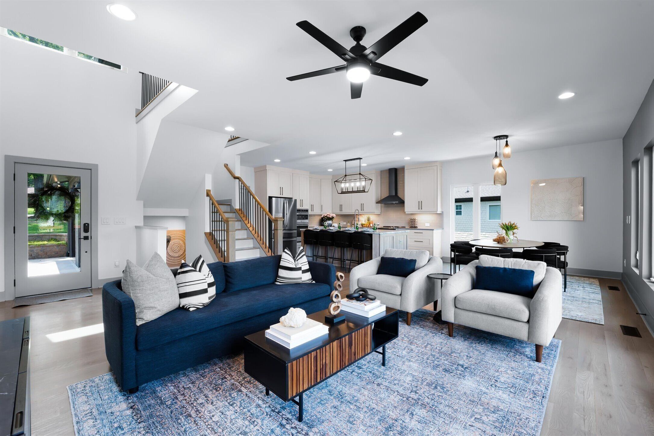 A spacious living area with a blue sofa, a white armchair, and a coffee table. A ceiling fan and pendant lights are visible.
