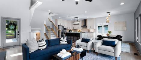 A spacious living area with a blue sofa, a white armchair, and a coffee table. A ceiling fan and pendant lights are visible.