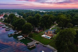 An aerial view of a lakeside property with a large house, dock, and swimming pool.