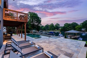 A poolside area with lounge chairs and a wooden deck overlooking a lake.