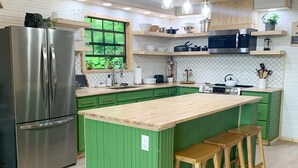 Eine moderne Küche mit grünen Schränken, einem Edelstahlkühlschrank, Holzstühlen und einem großen Fenster.