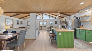 Eine moderne Küche mit Holzbalken, einer grünen Kochinsel, Barhocker und Blick durch die Fenster.
