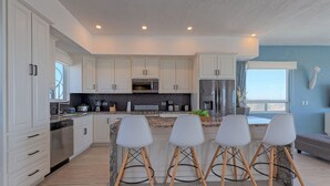 A modern kitchen with white cabinets, stainless steel appliances, and a central island with bar stools.