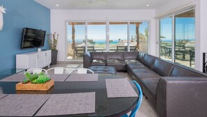 A modern living room with a large window, a ceiling fan, a flat-screen TV, and a leather sofa.