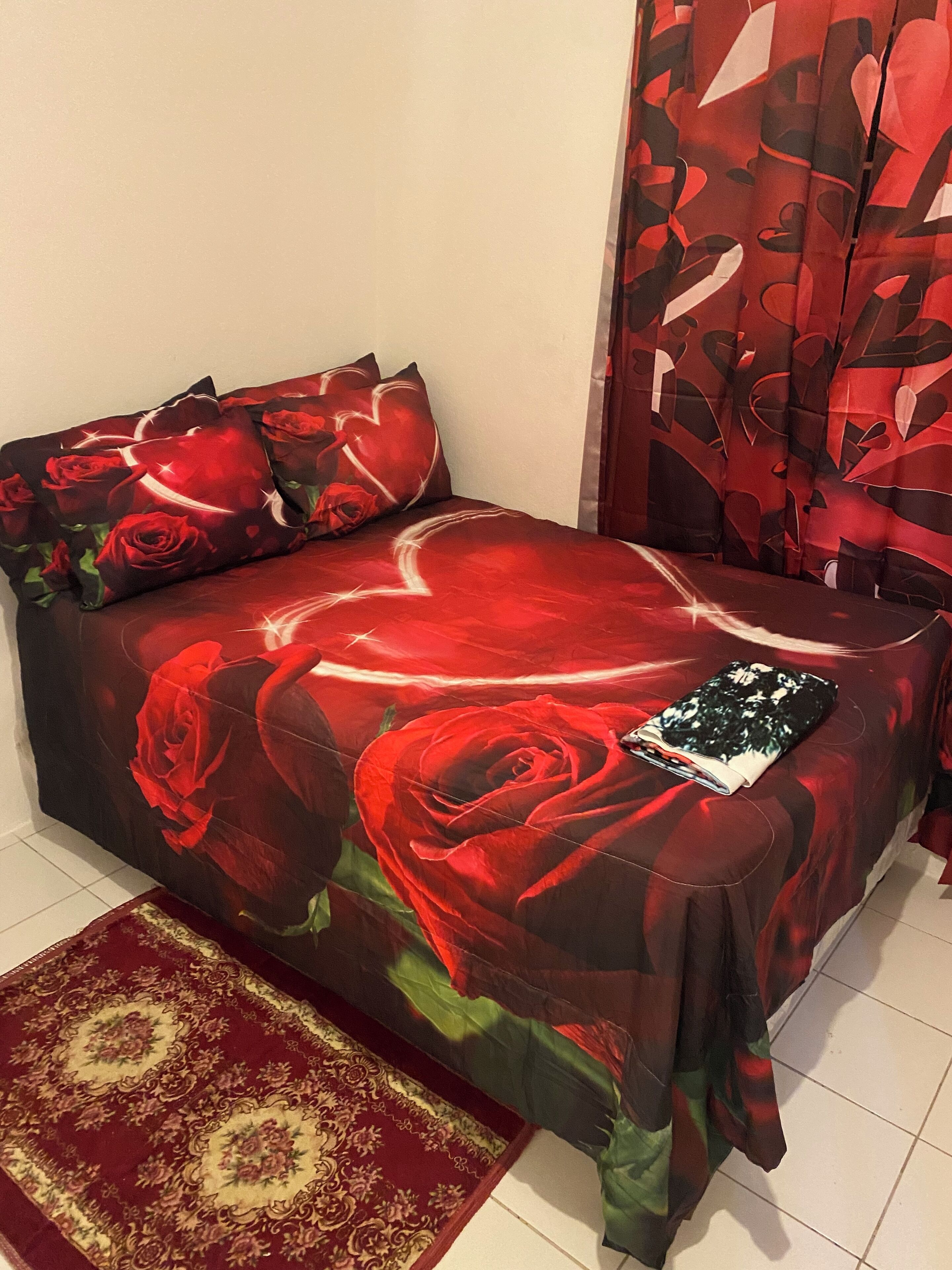 A bed with a red floral bedspread, a matching pillow, and a red and green rug.