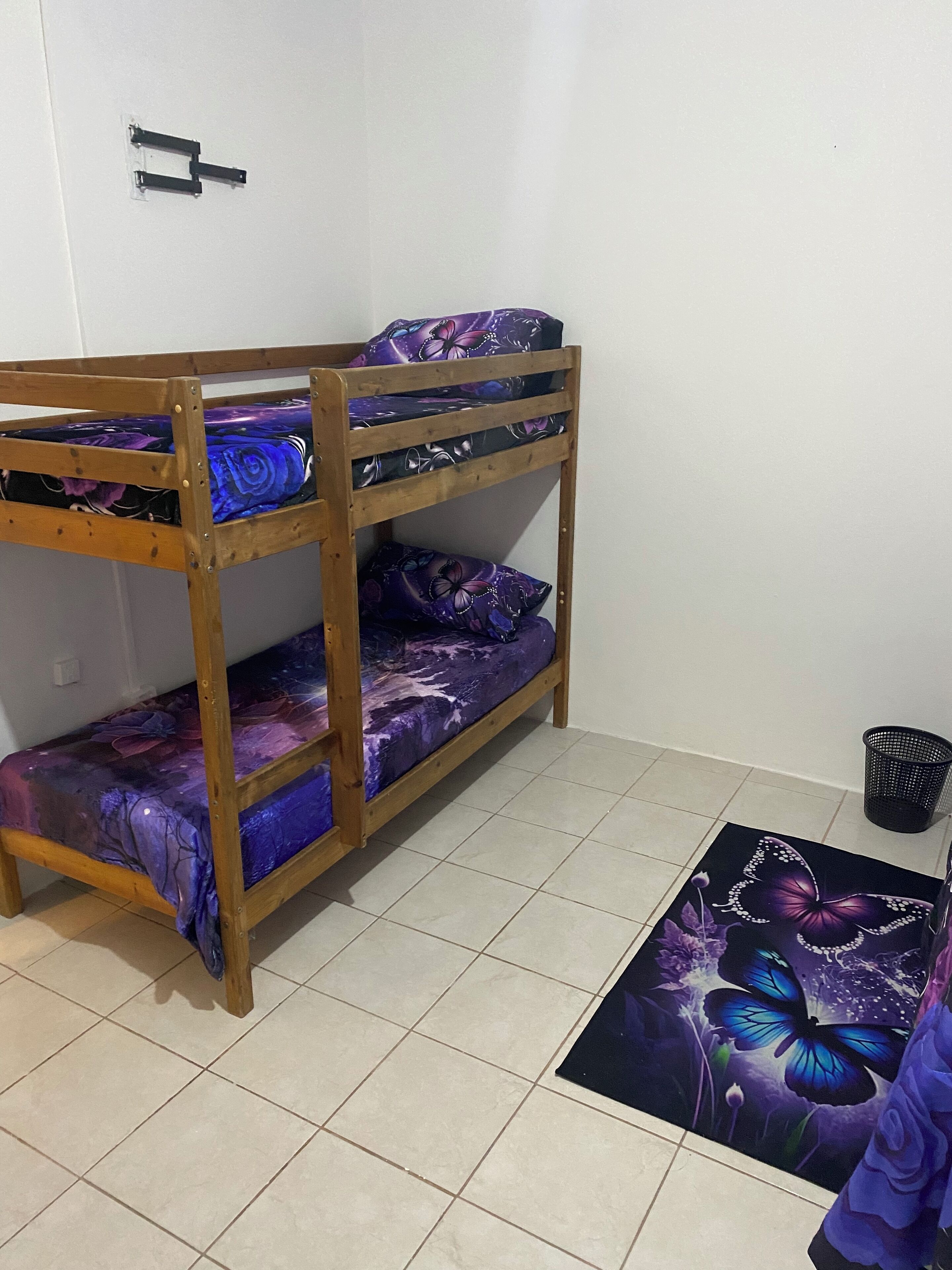 A bunk bed with a purple floral bedspread, a tiled floor, and a black trash bin.