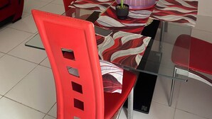 Un coin repas avec une table en verre, des chaises rouges, une plante en pot et un téléviseur fixé au mur.