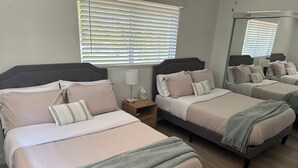 Een slaapkamer met twee bedden, elk met hoofdeinde, een nachtkastje met lamp en een raam met zonwering.